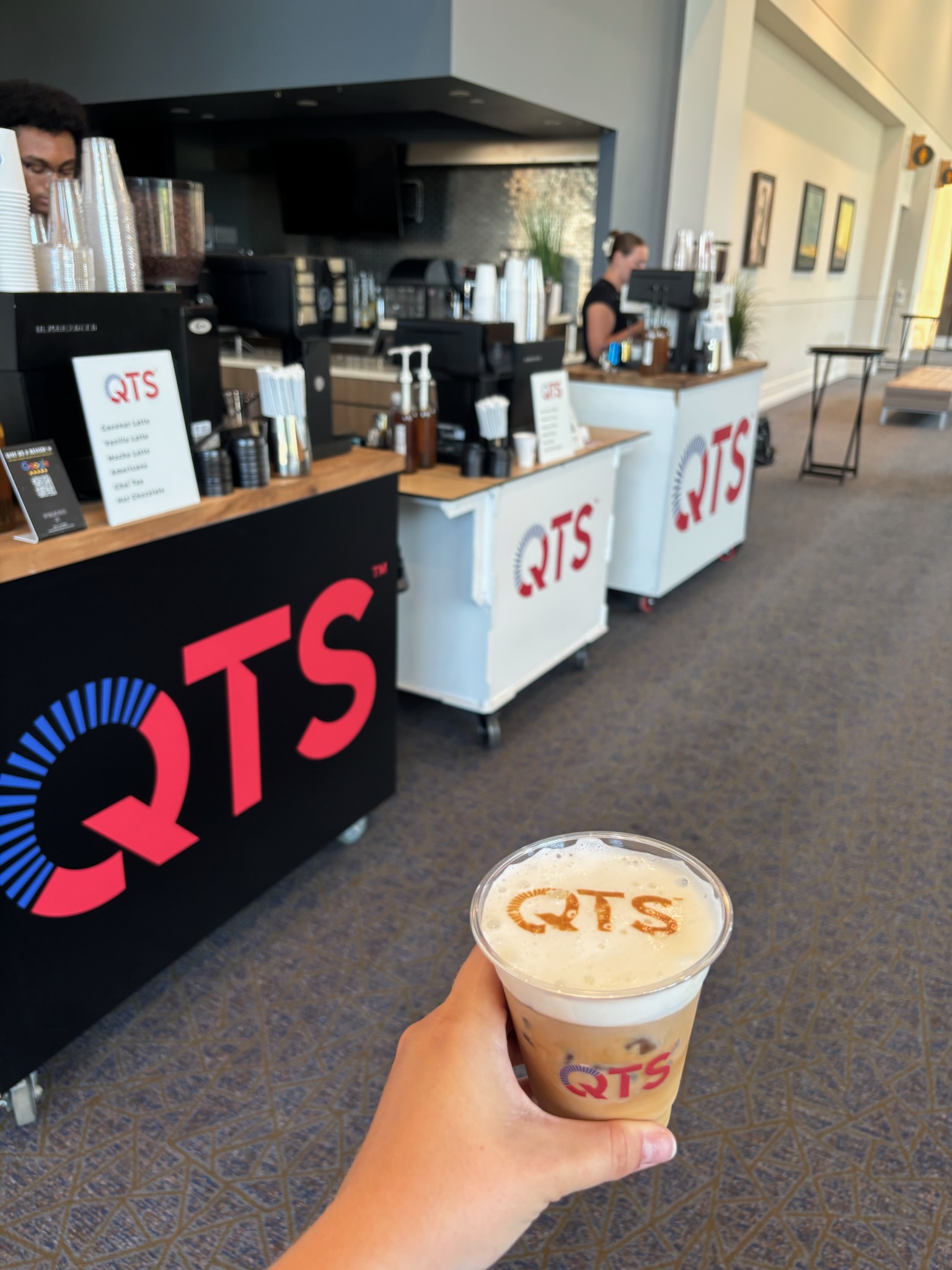 Custom QTS latte displayed in front of three branded coffee carts at Overland Park Convention Center