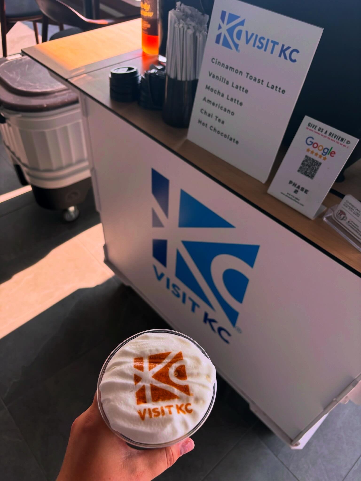 Custom Visit KC latte displayed in front of the branded coffee cart for an employee appreciation event